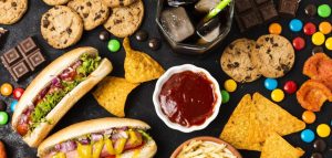 Різноманітні нездорові продукти на чорному тлі: хот-доги, печиво, чіпси, шоколад і цукерки