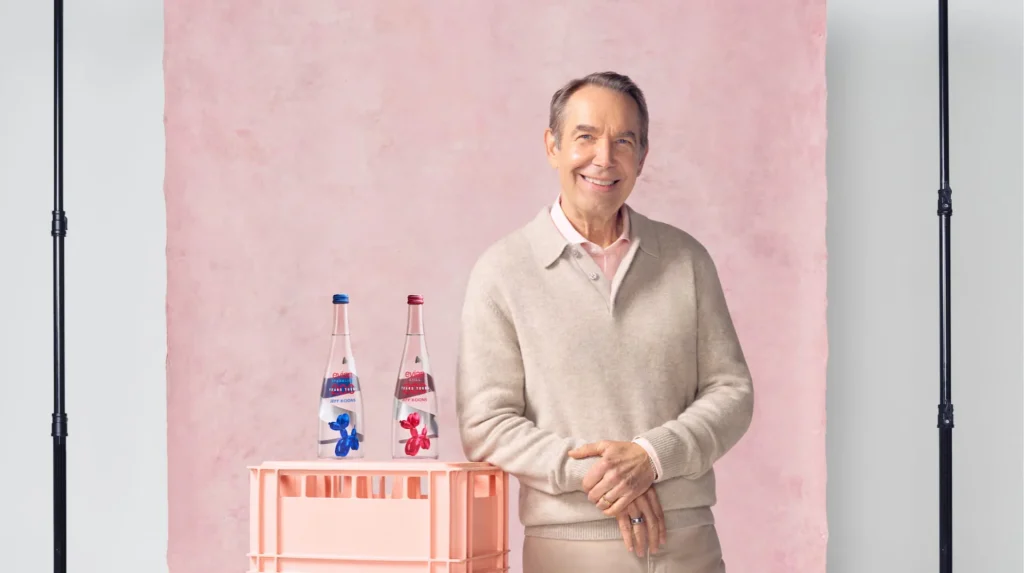 Усміхнений Джефф Кунс біля рожевої скриньки з пляшками Evian і собаками-кульками