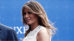 Меланія Трамп у білій мереживній сукні посміхається на синьому тлі