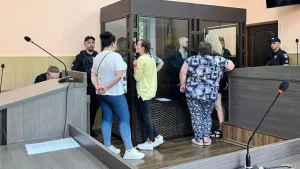 Жінки біля скляної клітки з обвинуваченими у залі суду під охороною поліції