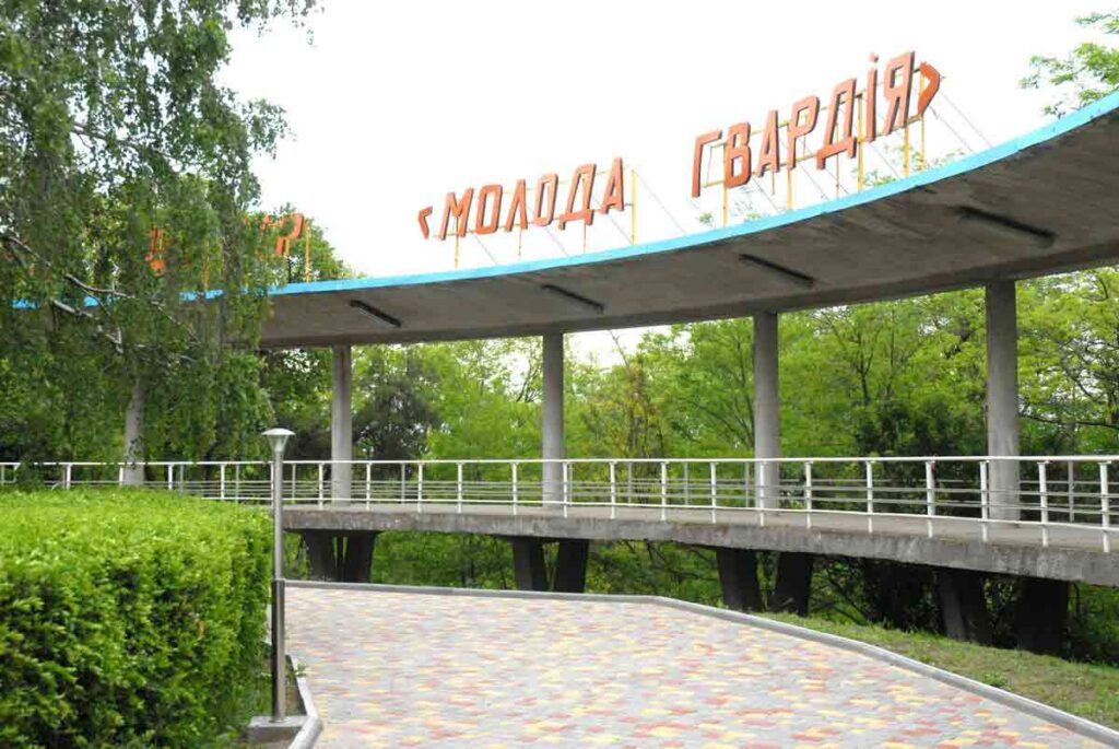 Бетонний павільйон з помаранчевою вивіскою Молода гвардія над доріжкою серед зелені
