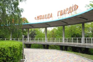 Бетонний павільйон з помаранчевою вивіскою Молода гвардія над доріжкою серед зелені