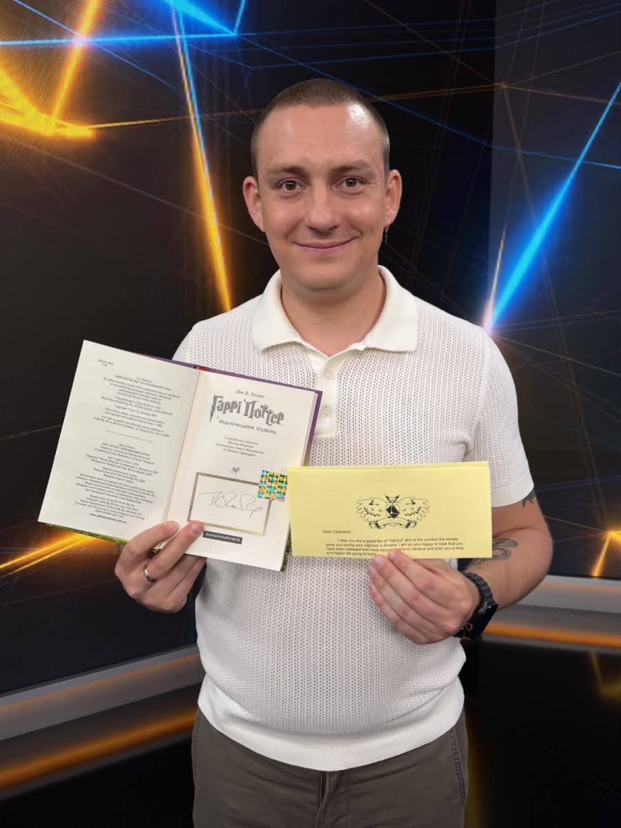 Усміхнений чоловік тримає відкритий підписаний Гаррі Поттер і жовтий конверт з листом