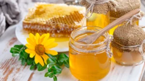 Банки з медом, стільники, деревяна ложка та жовта квітка на столі