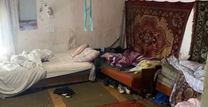 Неохайна кімната з ліжками, килимами на стінах і розкиданим одягом на підлозі