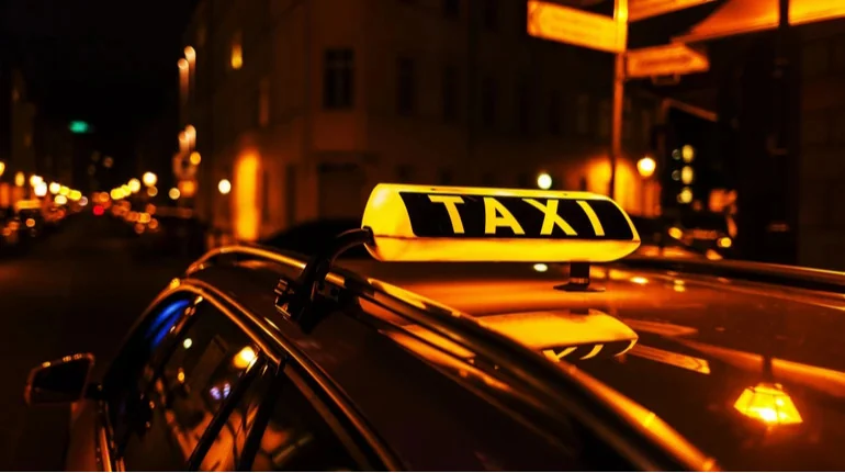 Освітлений жовтий знак TAXI на даху авто вночі на міській вулиці