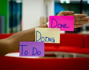 Рука тримає кольорові стікери To Do, Doing і Done на фоні офісу